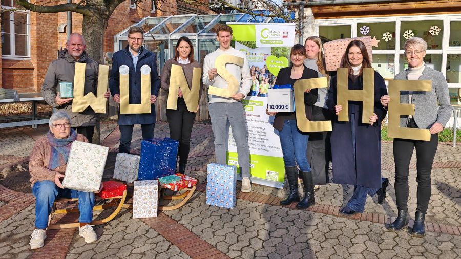 Das Foto zeigt eine Gruppe Menschen, die goldene Buchstaben hochhalten und einige Geschenke. Die Buchstaben bilden das Wort "Wünsche".