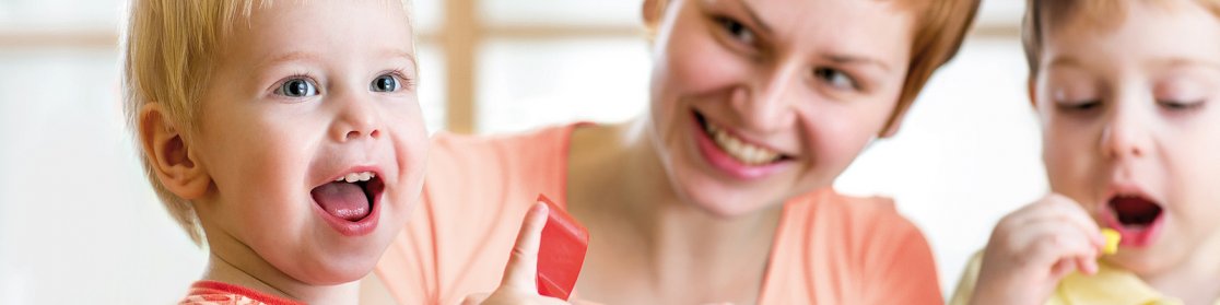 Das Bild zeigt zwei Kinder beim Spielen, die von einer Frau betreut werden.